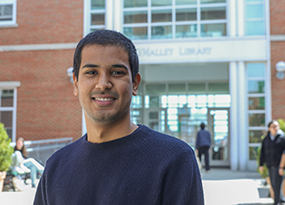 male student with dark hair in front of campus library