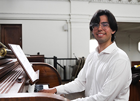 male student with dark hair and glasses sitting at piano