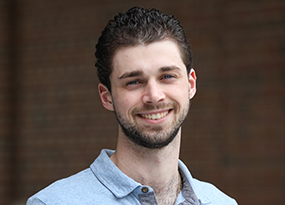 male student with beard in front of campus archways