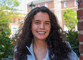 female student with dark hair standing by bricks on campus