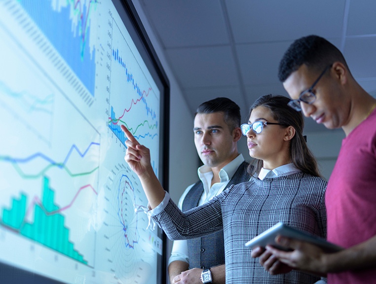 Finance students standing in front of a visual screen.