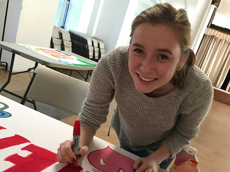 female student designing sign and smiling at camera