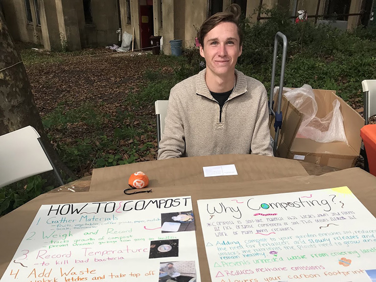 male student sitting at table outside in front of two posters