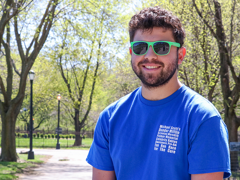 man with sunglasses stands in front of park on sunny day