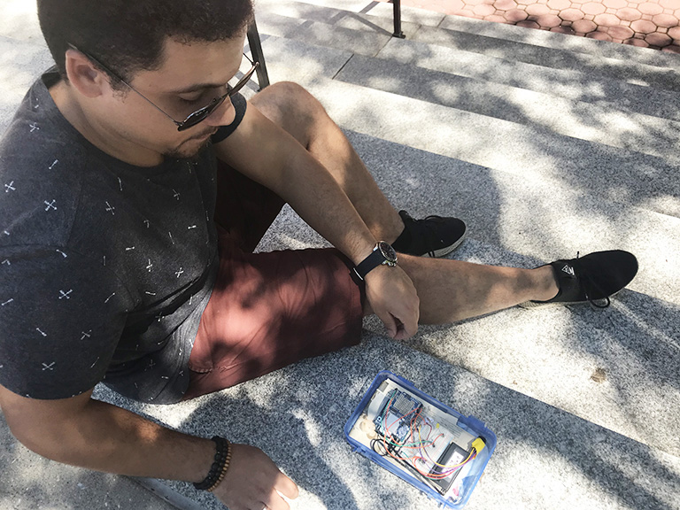 Student Jovan Gonzales sitting on concrete with an device that collects air samples