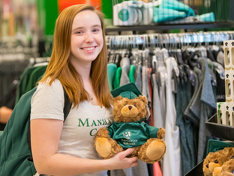 Ellen Farrelly smiling in Manhattan College's bookstore holding a teddy bear dressed in a graduation gown.