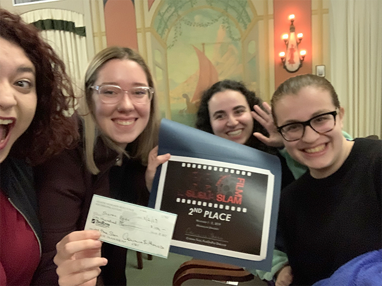 Four students holding up their festival winning award certifcate and prize check, smiling.