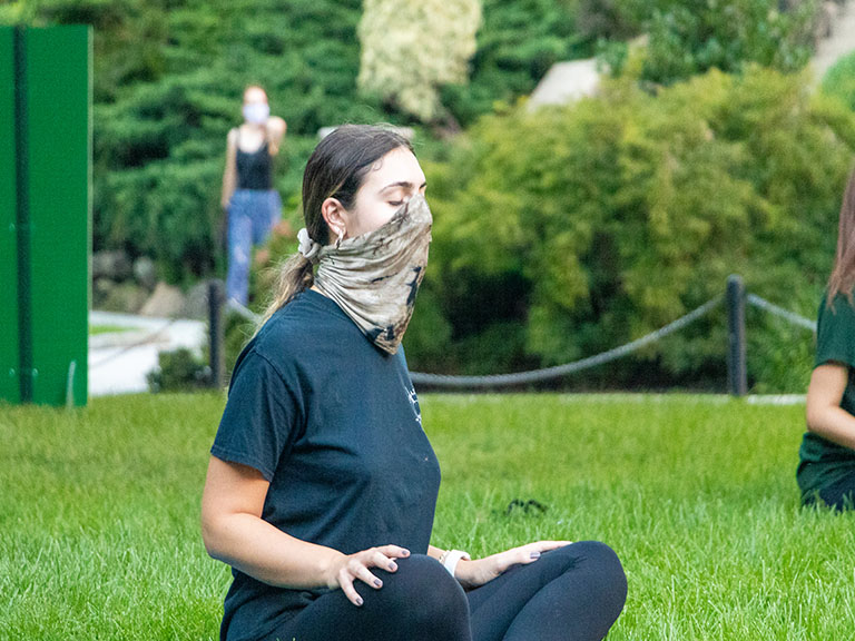 woman wearing mask with eyes closed while sitting in cross legged position outside