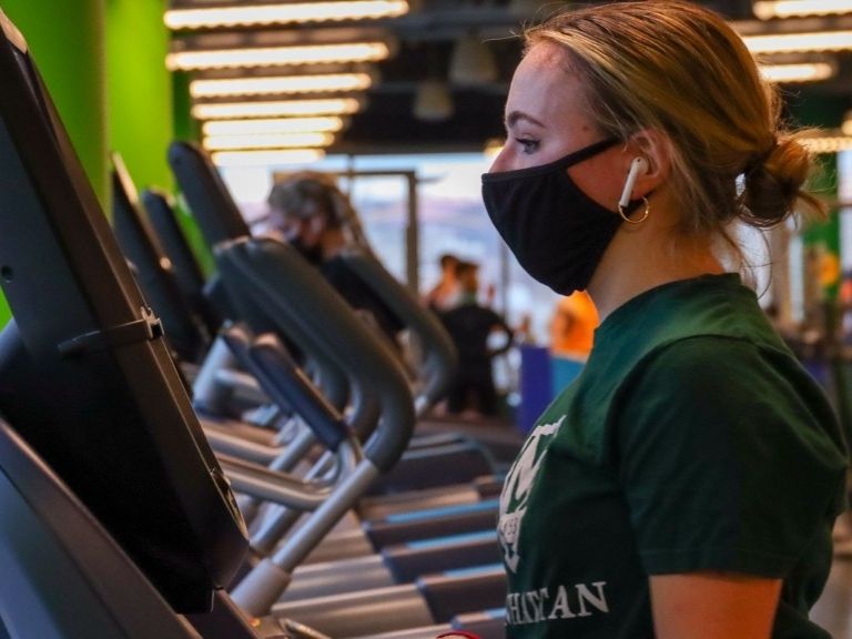 young woman runs on treadmill wearing face covering