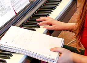 female student writing in notebook balanced on music keyboard