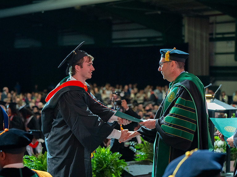 A male student shaking hands with President Riverso after receiving his diploma 