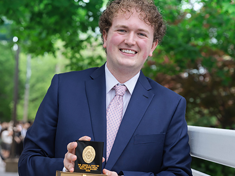 William Walker '26 poses outdoors holding the Joseph J. Gunn '30 Alumni Medal awarded by Manhattan University for leadership and service to the University community.