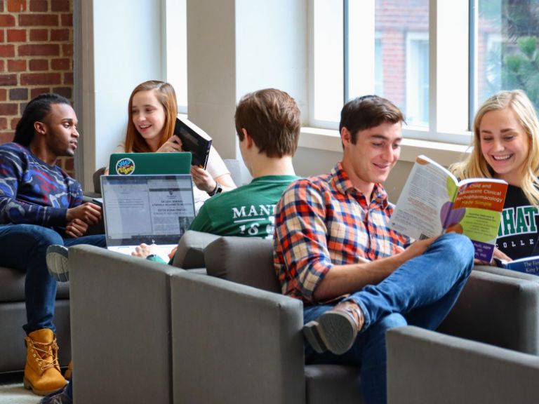 male student in plaid shirt reads book alongside female student in library